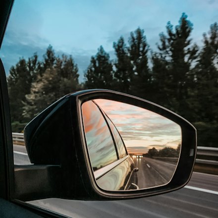 Side mirror reflecting traffic on a highway at dusk