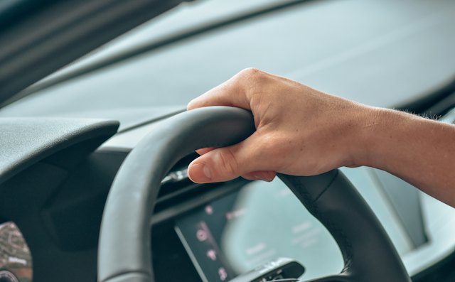 Driver's hand resting on the steering wheel of a modern car