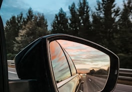 Side mirror reflecting traffic on a highway at dusk