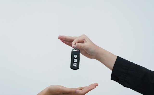 One hand passing a car key to another against a pale background