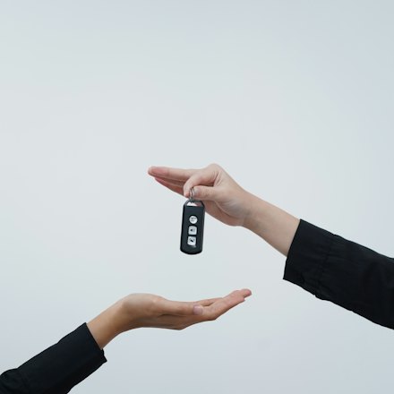 One hand passing a car key to another against a pale background