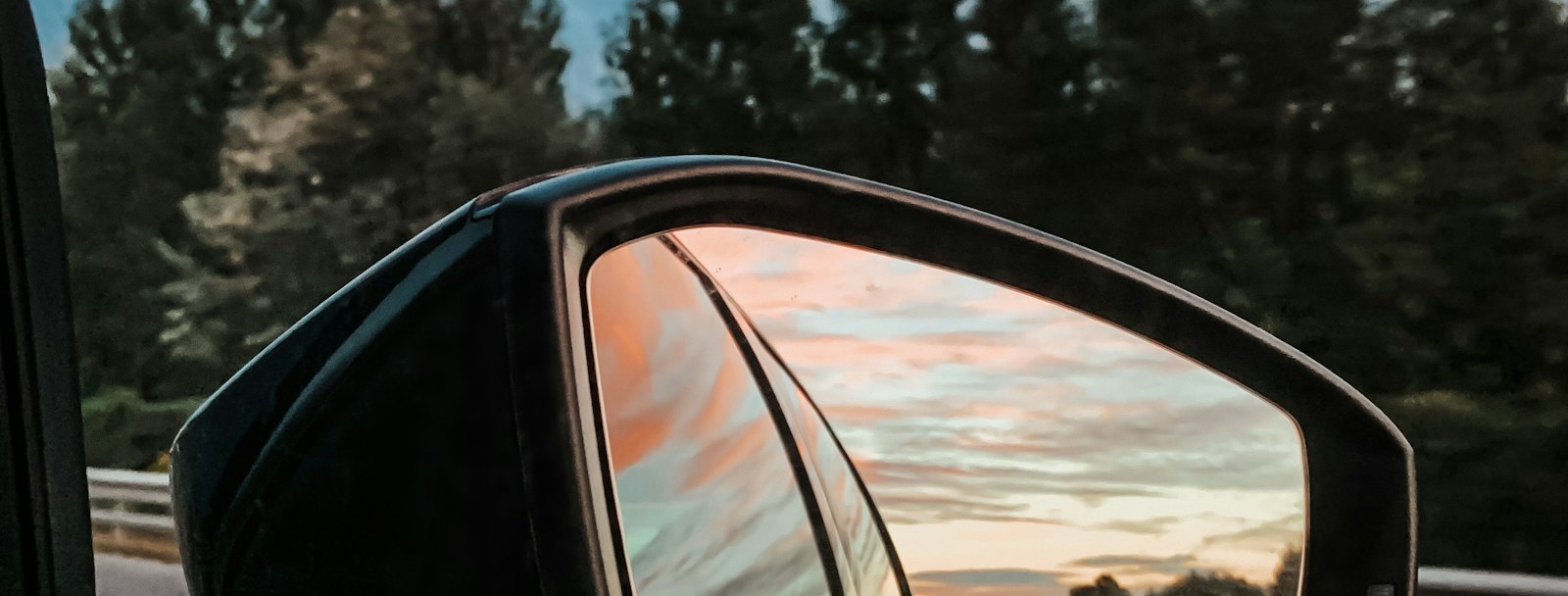 Side mirror reflecting traffic on a highway at dusk