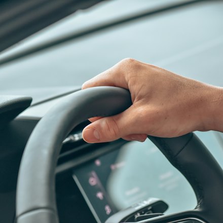 Driver's hand resting on the steering wheel of a modern car