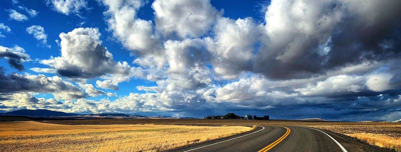 Open highway curving through golden prairie fields under a big cloudy sky