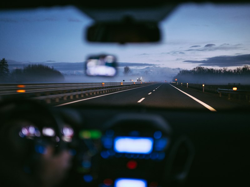 Dashboard lights and a divided highway at dusk seen from the driver's seat