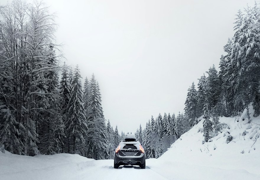 Car travelling along a snow-covered road between spruce trees