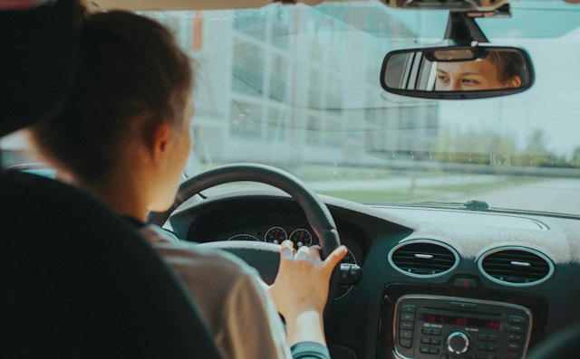 Learner driver checking the rear-view mirror with both hands on the wheel