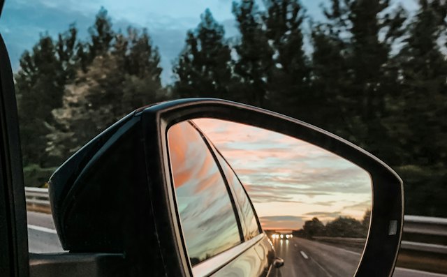 Side mirror reflecting traffic on a highway at dusk