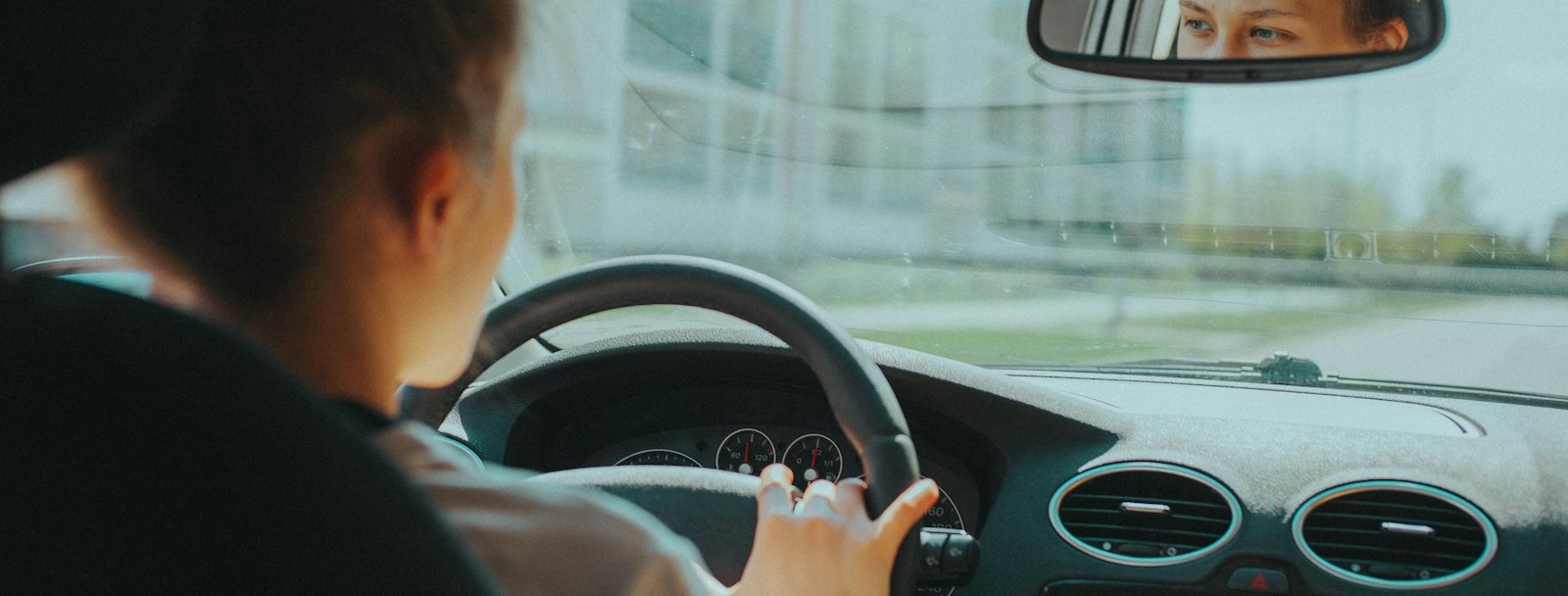 Learner driver checking the rear-view mirror with both hands on the wheel