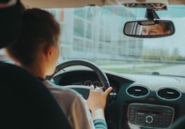 Learner driver checking the rear-view mirror with both hands on the wheel