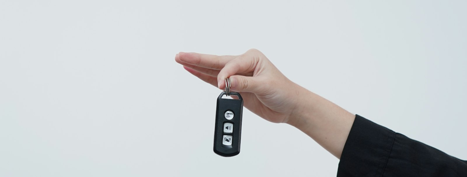 One hand passing a car key to another against a pale background
