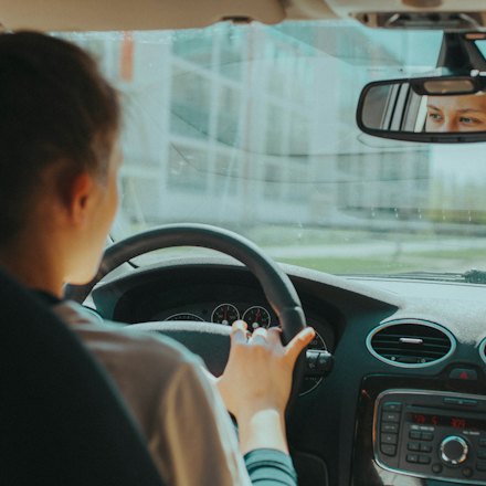Learner driver checking the rear-view mirror with both hands on the wheel