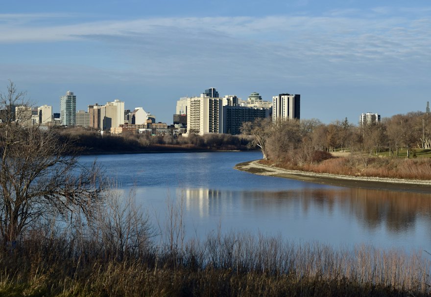 Downtown Winnipeg skyline reflected in a calm river under a blue sky