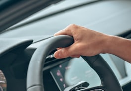 Driver's hand resting on the steering wheel of a modern car