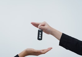 One hand passing a car key to another against a pale background