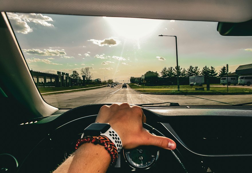 Driver's view of a sunny city road with one hand on the wheel